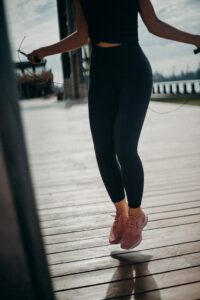 A woman exercising outdoors by jumping rope on a sunny day.