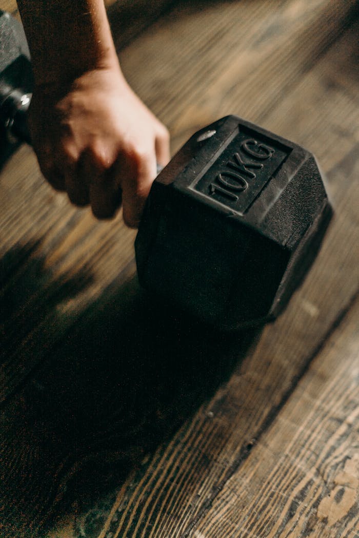A close-up shot of a hand gripping a 10kg dumbbell on a wooden floor, perfect for fitness themes.